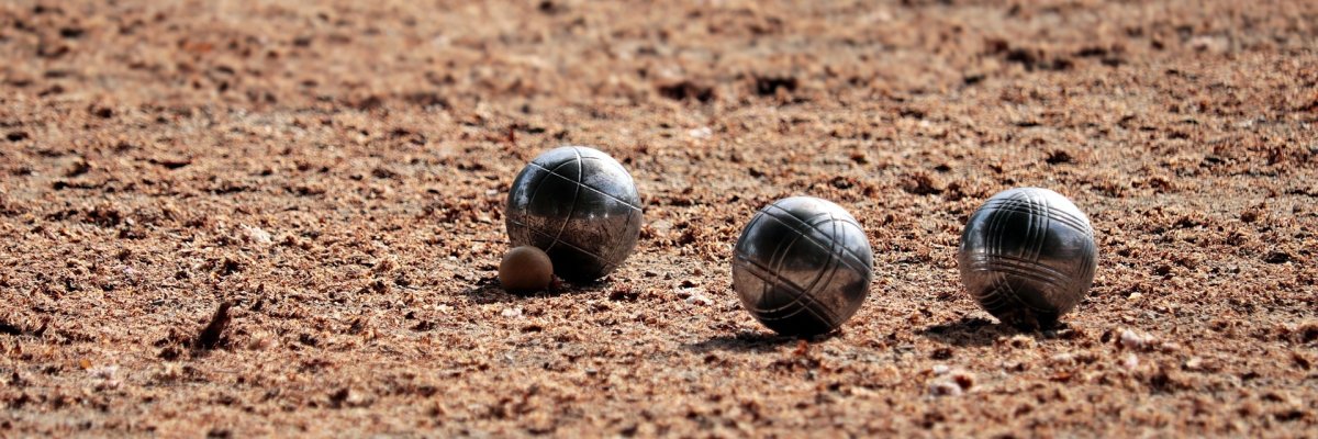 drei Boulekugeln nebeneinander auf einer Aschebahn
