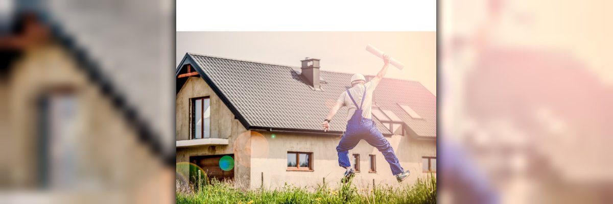 Mann springt vor Freude in die Luft. Im Hintergrund sieht man ein neu gebautes Haus.