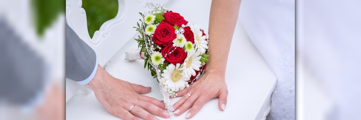 Hochzeit Hände zweier Ehepartner mit Ehering und Brautstrauß