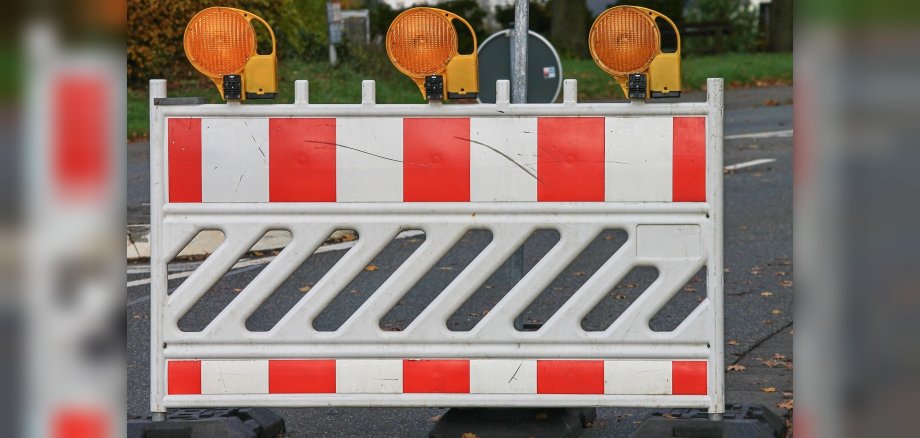 Foto eines rot-weiß gestreiften Schrankenzaun mit drei gelben Blitzleuchten